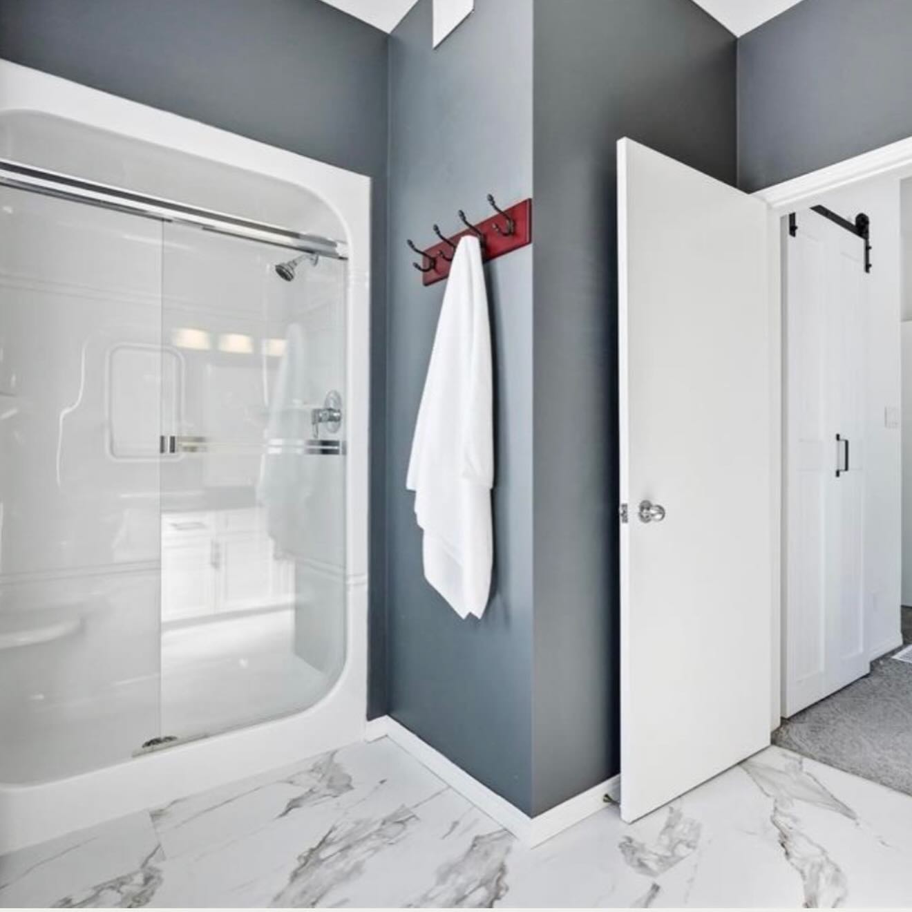 Bathroom after the floor refresh, with white marble-look tile, deep grey walls, a white glass shower, and a red wood hook rail