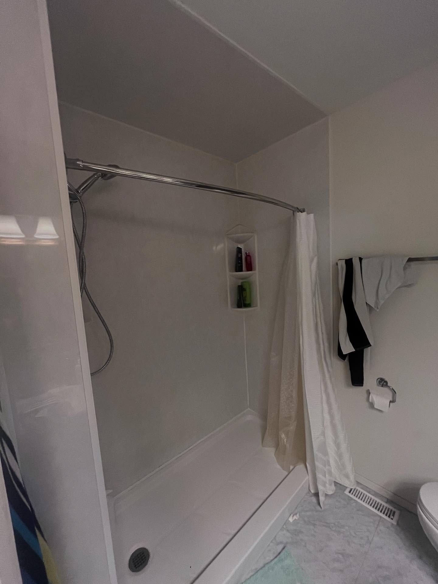 Bathroom shower before renovation, with a standard white surround, chrome handheld shower, and marble-look flooring