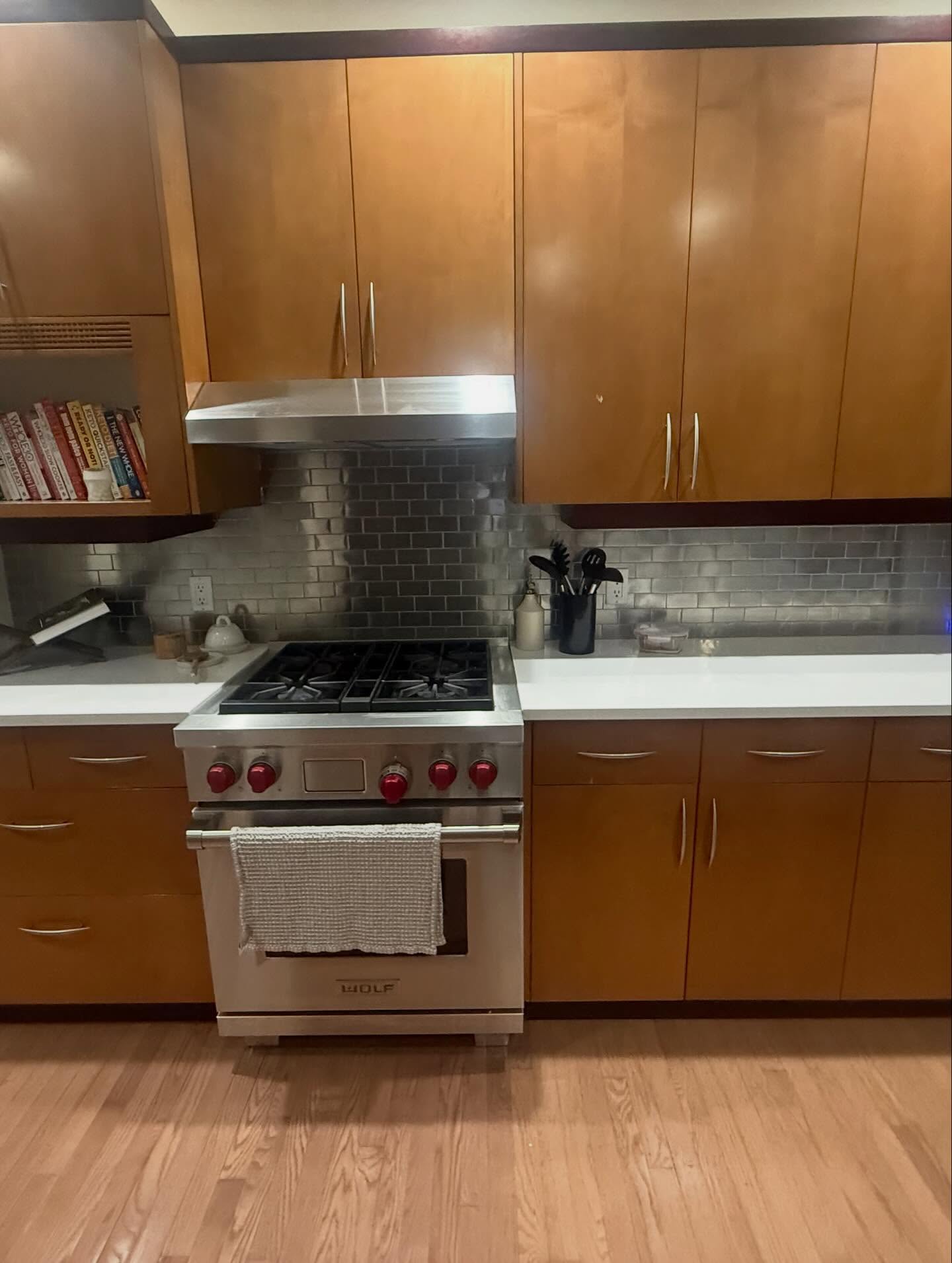 Project Lily cooking wall before the renovation, with warm wood cabinets, metallic subway tile, and a stainless Wolf range