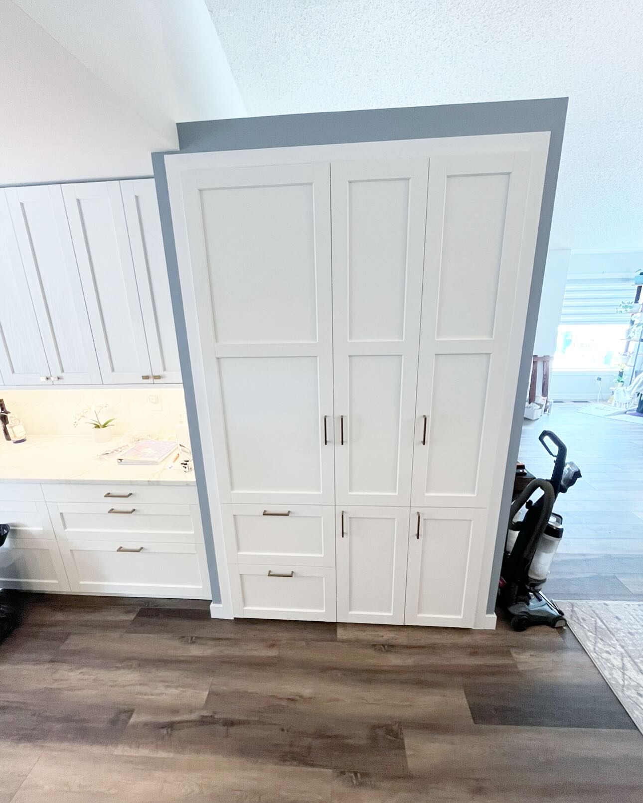 Finished tall white Shaker pantry wall with drawers, cupboard doors, and a blue-grey wall beside a white kitchen counter