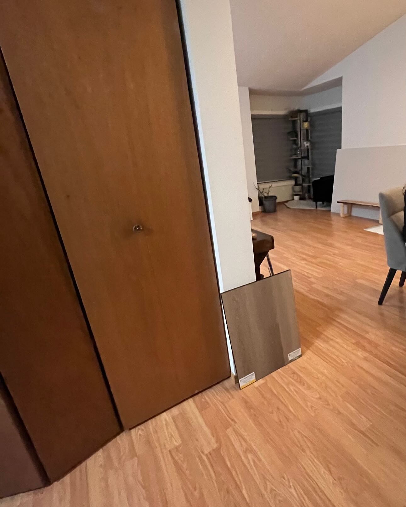 Starting-point view of an adjoining room with existing wood closet doors and a wood-look flooring sample leaning against the wall