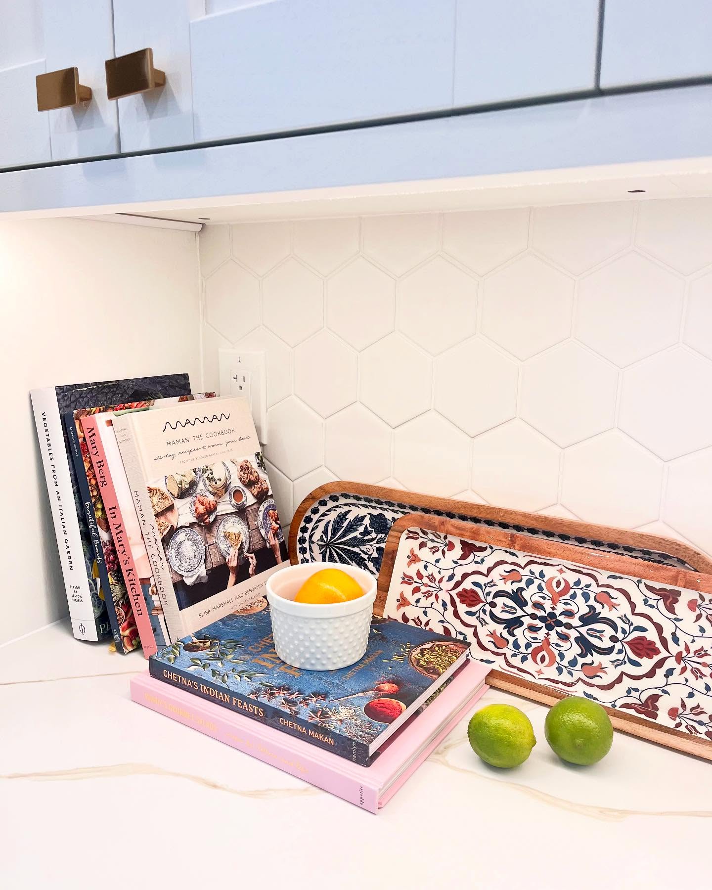 Close view of Project Daisy white hexagon tile, veined counter, brass knobs, and cookbooks
