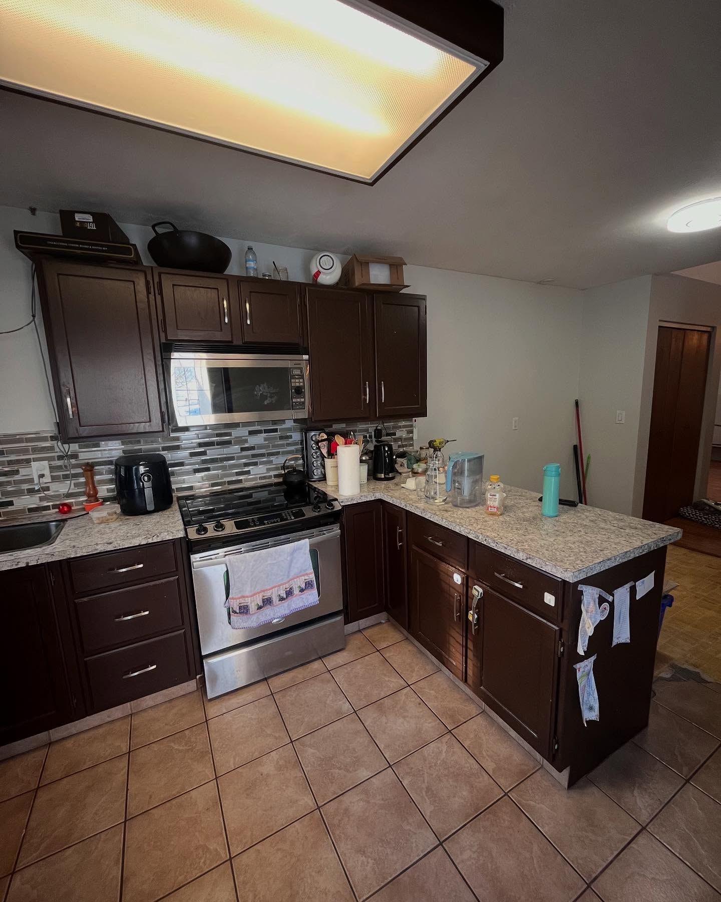 Project Daisy range wall before renovation, with dark wood cabinets, mosaic tile, and beige floor tile