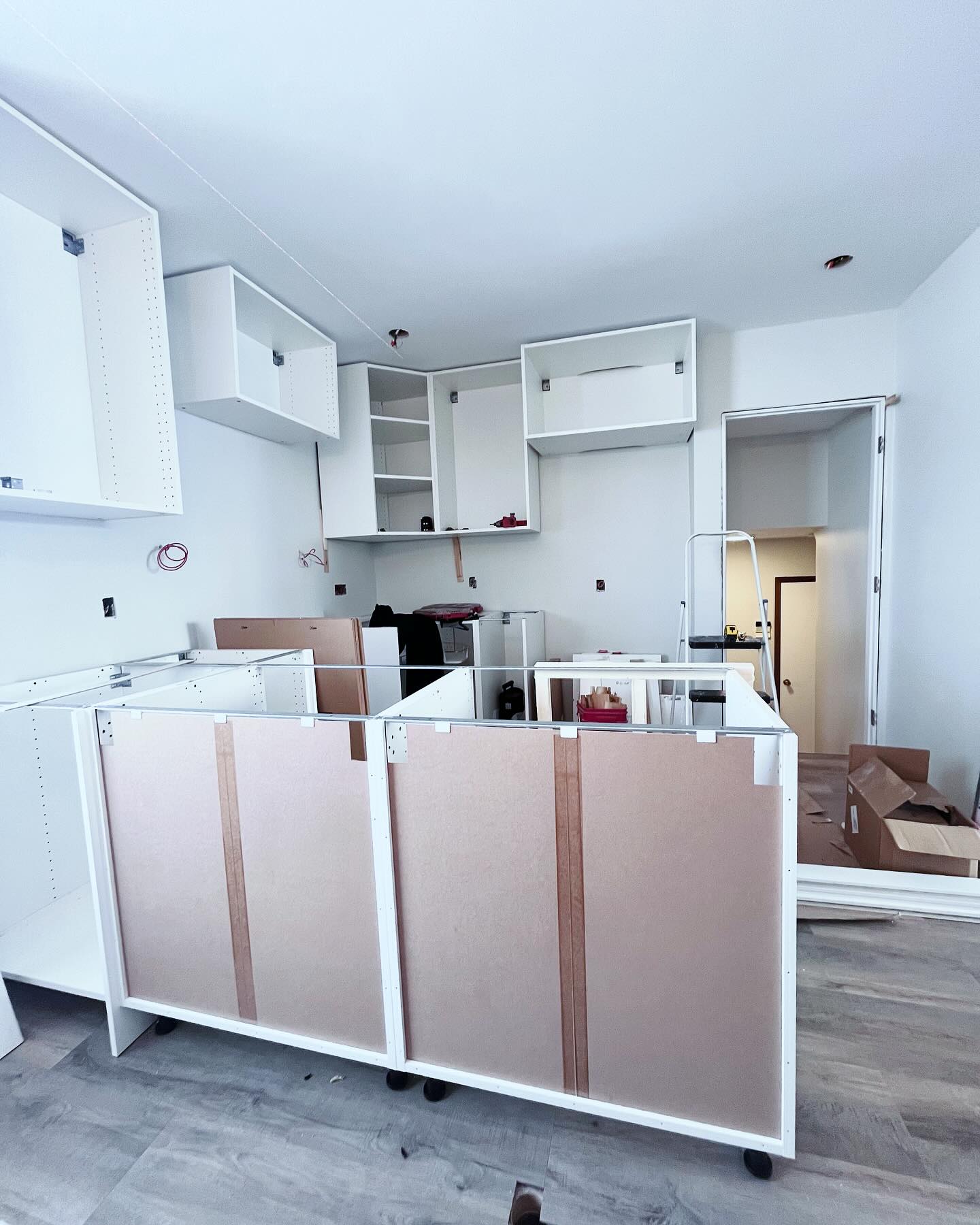 Project Rose kitchen in progress with white cabinet boxes, open backs, and tools still on the new plank floor