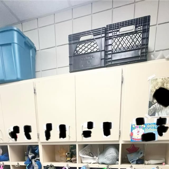 Daycare storage wall before renovation with upper cabinets, open cubbies, hooks, and temporary bins