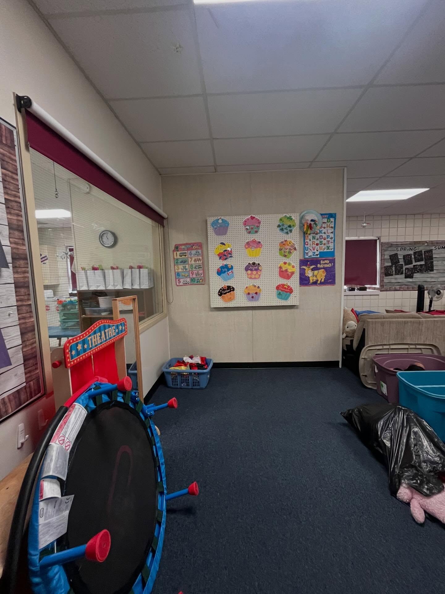 Daycare classroom before the refresh, with toys, bins, a puppet theatre, and materials gathered on a dark blue carpet