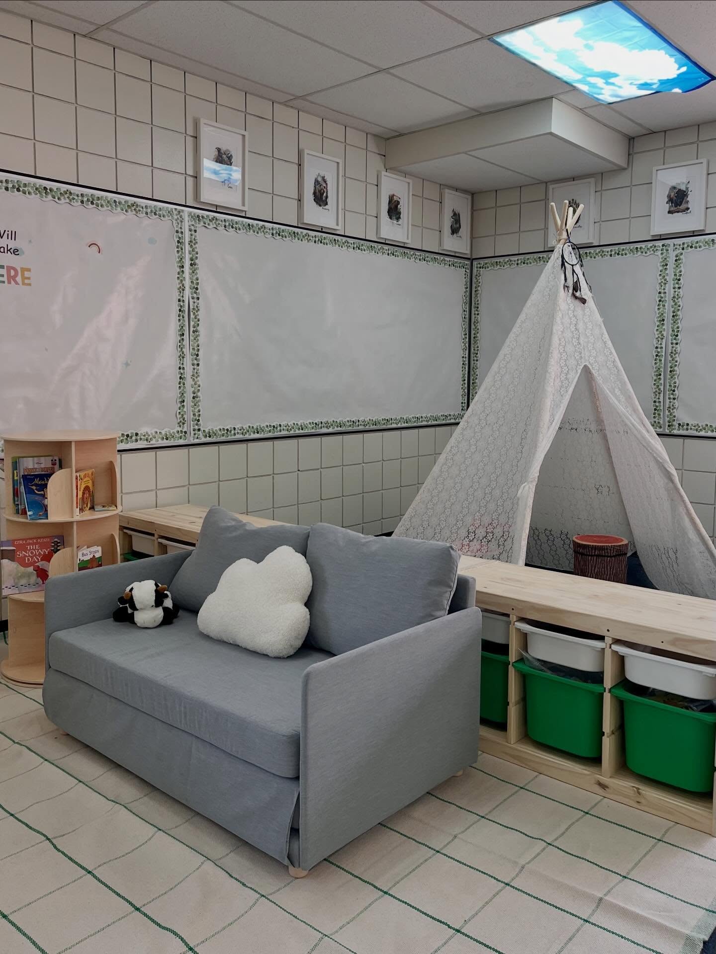 Finished daycare reading nook with a grey loveseat, lace teepee, low wood bins, and a green grid rug