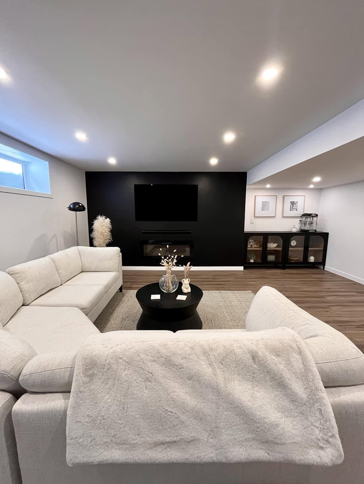 Finished basement lounge from our Winnipeg work, with a cream sectional and a black fireplace wall