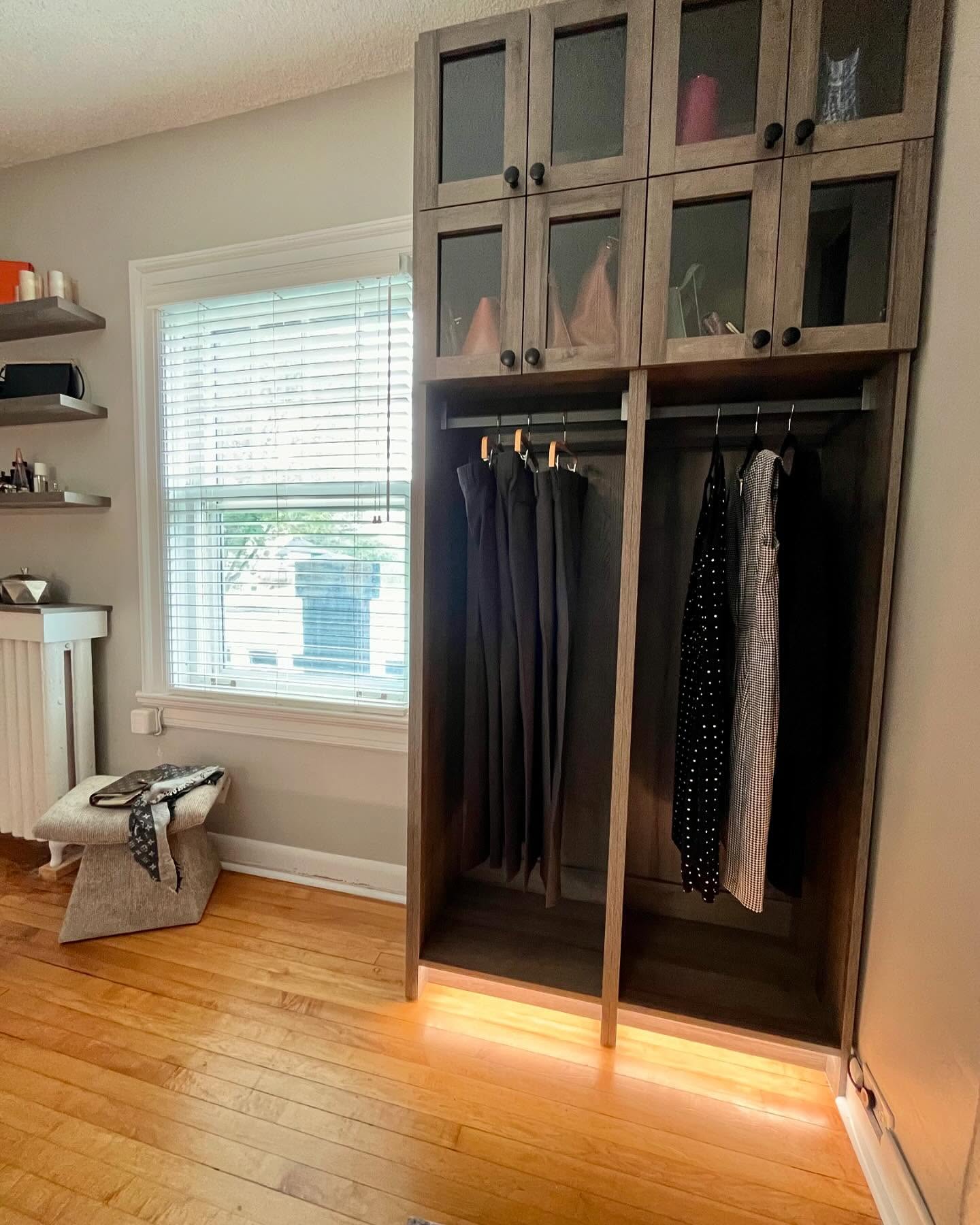 Finished custom closet from our Winnipeg work, with wood cabinets, glass uppers, and warm toe-kick lighting