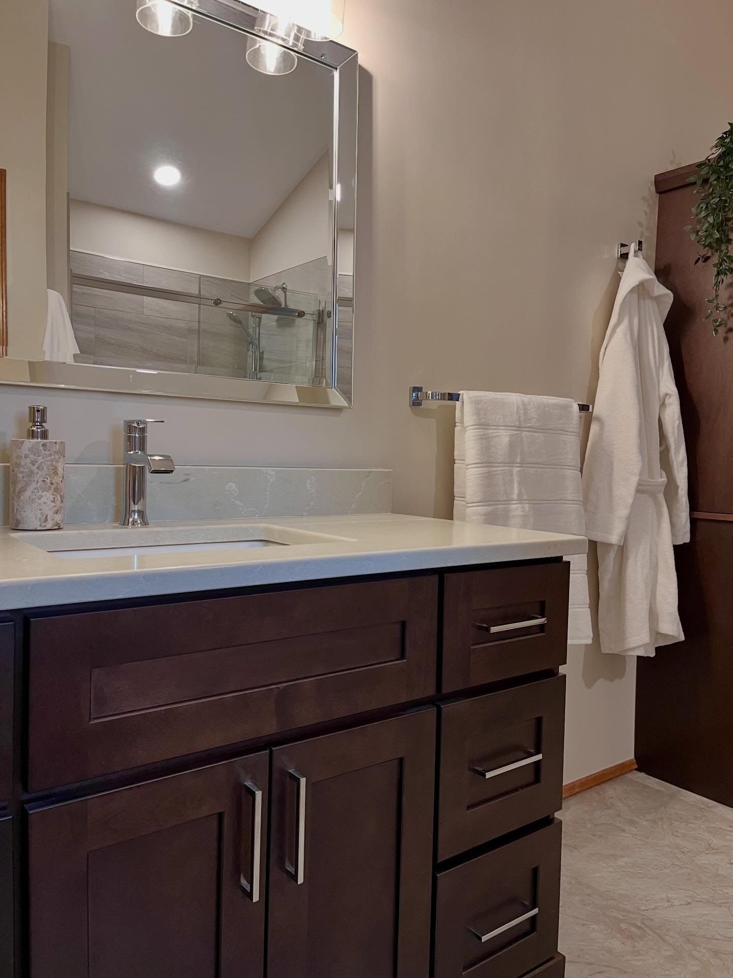 Bathroom vanity in dark wood with a white quartz top and a beveled mirror