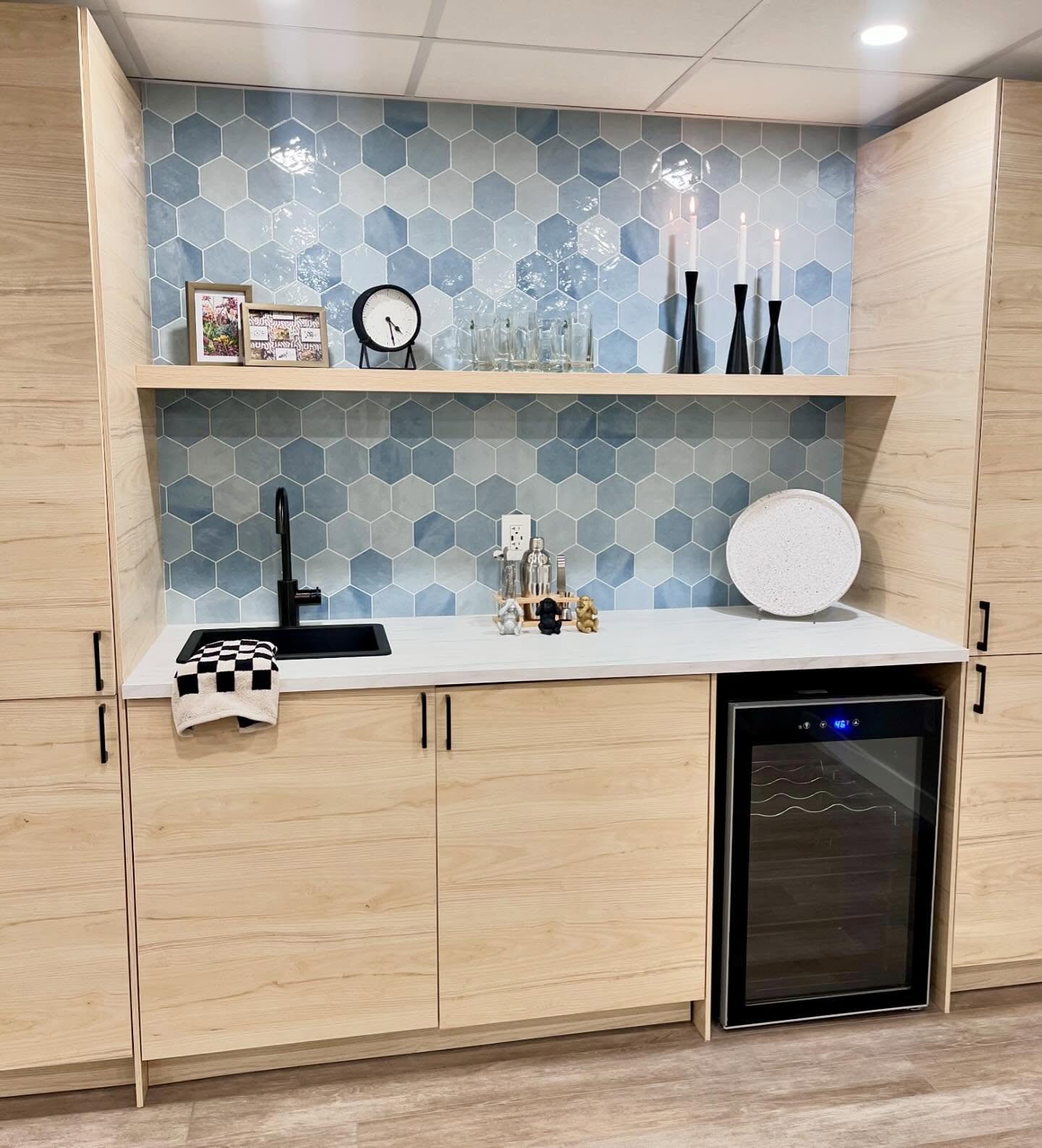 Wet bar with light wood cabinets, blue hexagon tile, and a glass-door beverage fridge