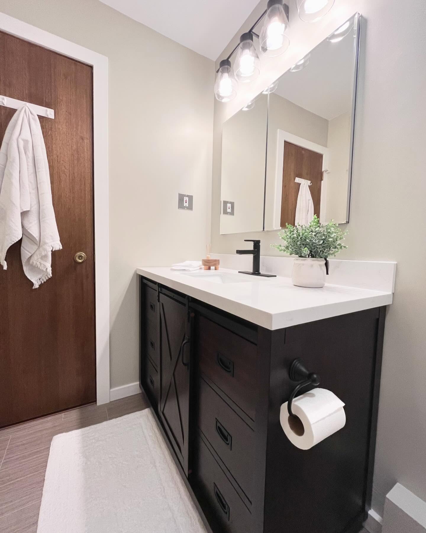 Finished bathroom with a dark wood vanity, black faucet, wide mirror, floating shelves, and white tub curtain