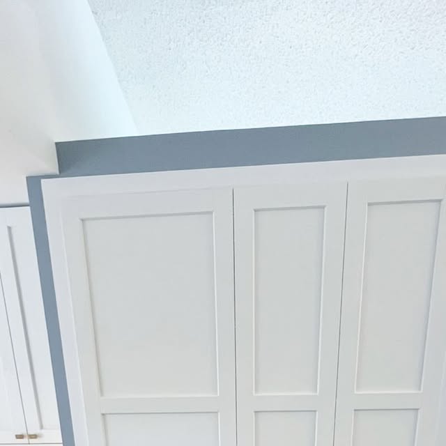 Close view of tall white Shaker cabinet doors meeting a deep blue-grey wall and a textured white ceiling