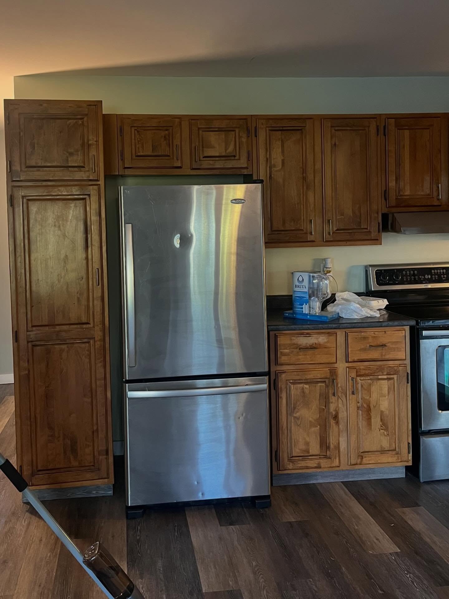 Before: honey-oak pantry and fridge wall with a dark laminate counter