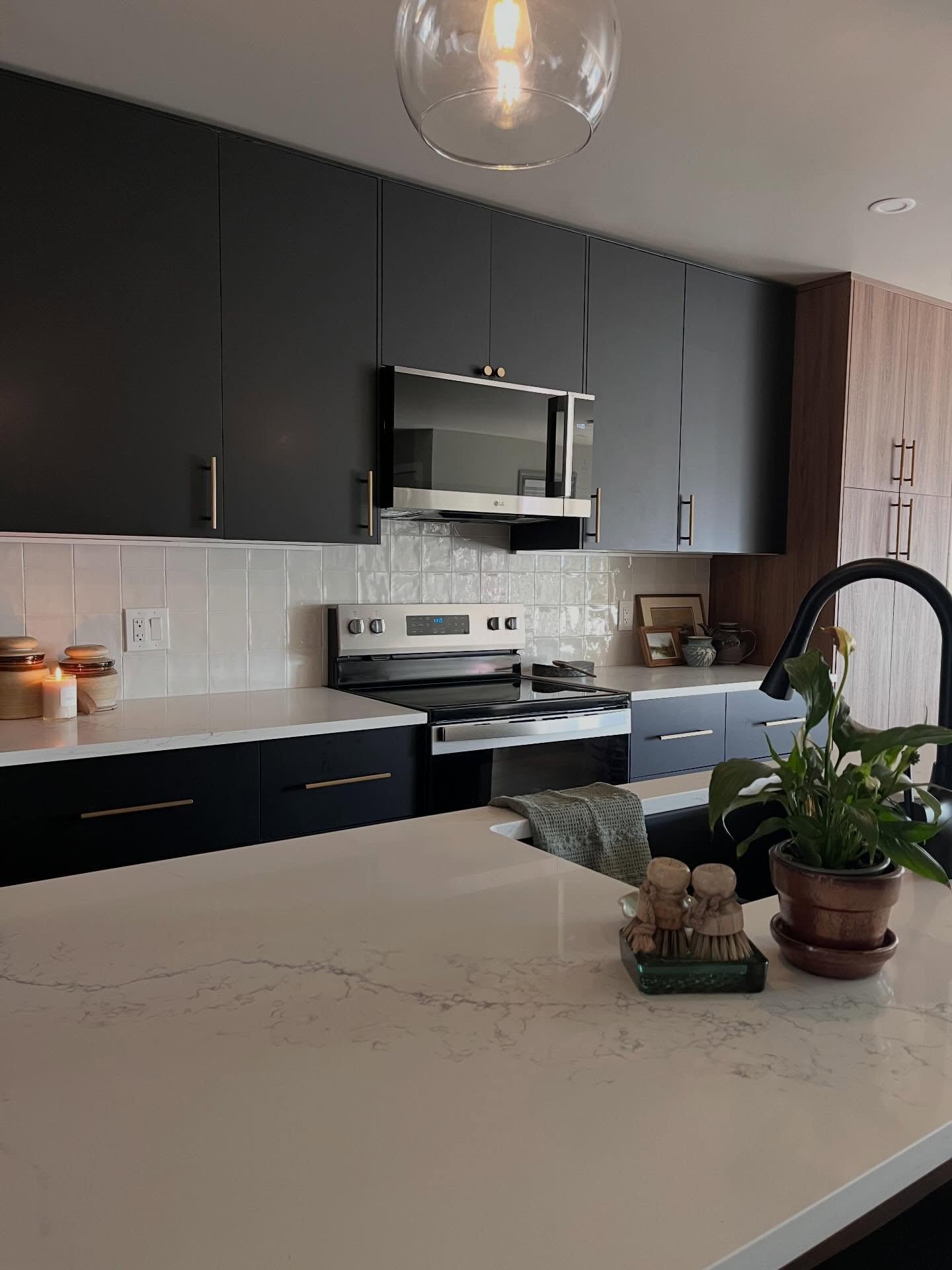 After: charcoal cabinets, gold pulls, white tile, and the island sink