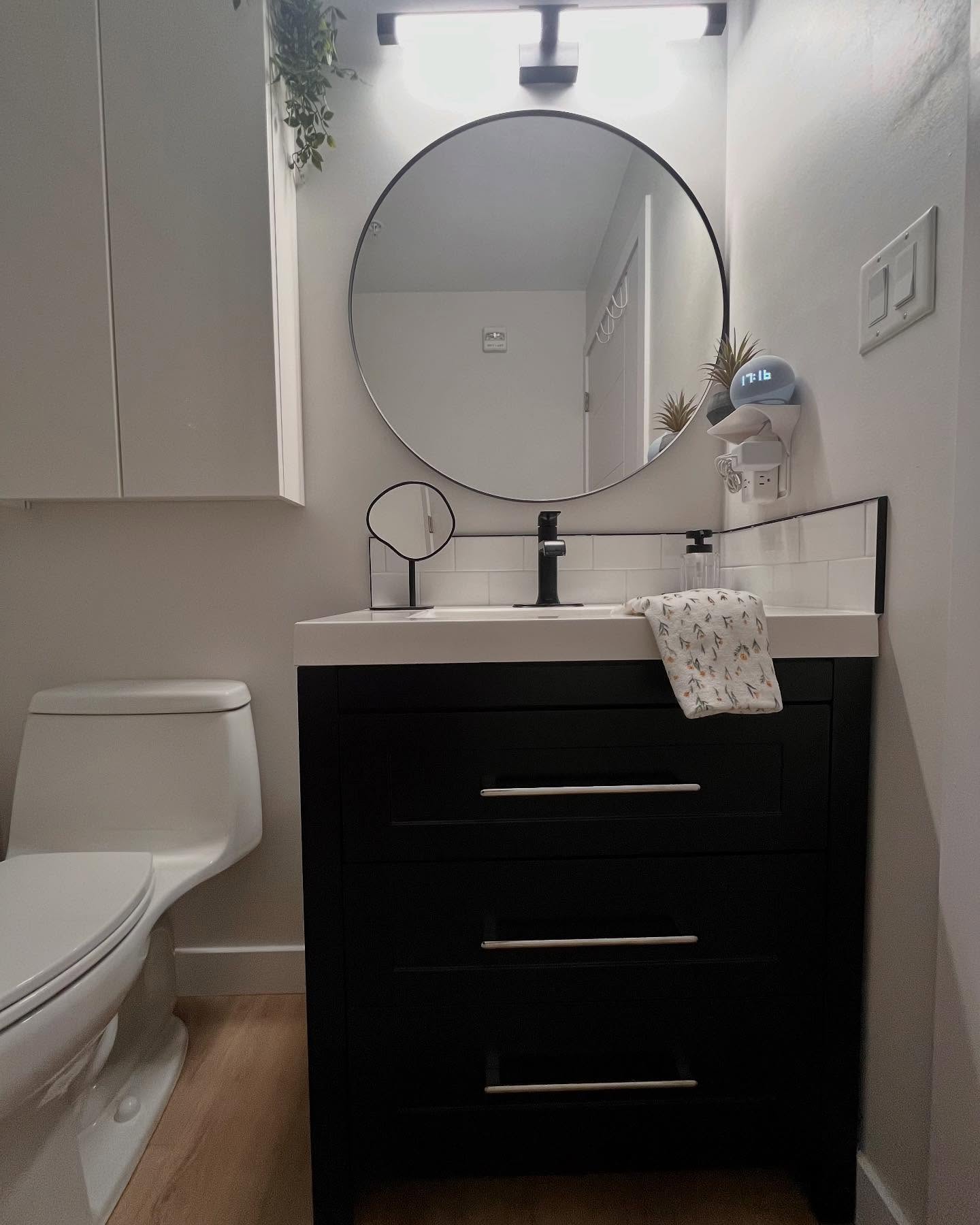 Project Lotus navy vanity with a circular black mirror, white tile backsplash, and matte black faucet