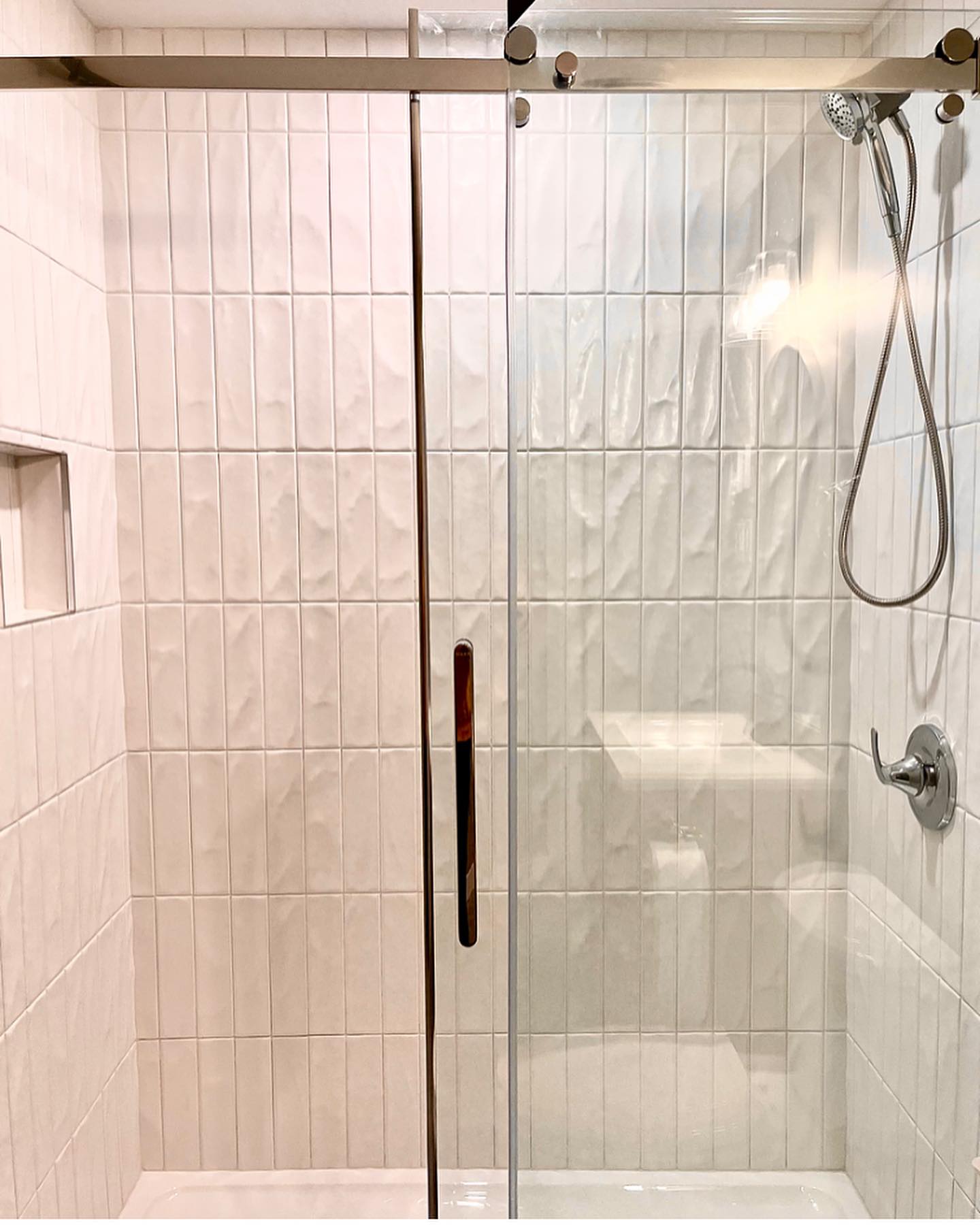 Walk-in shower with vertical textured tile, a glass sliding door, and chrome fixtures
