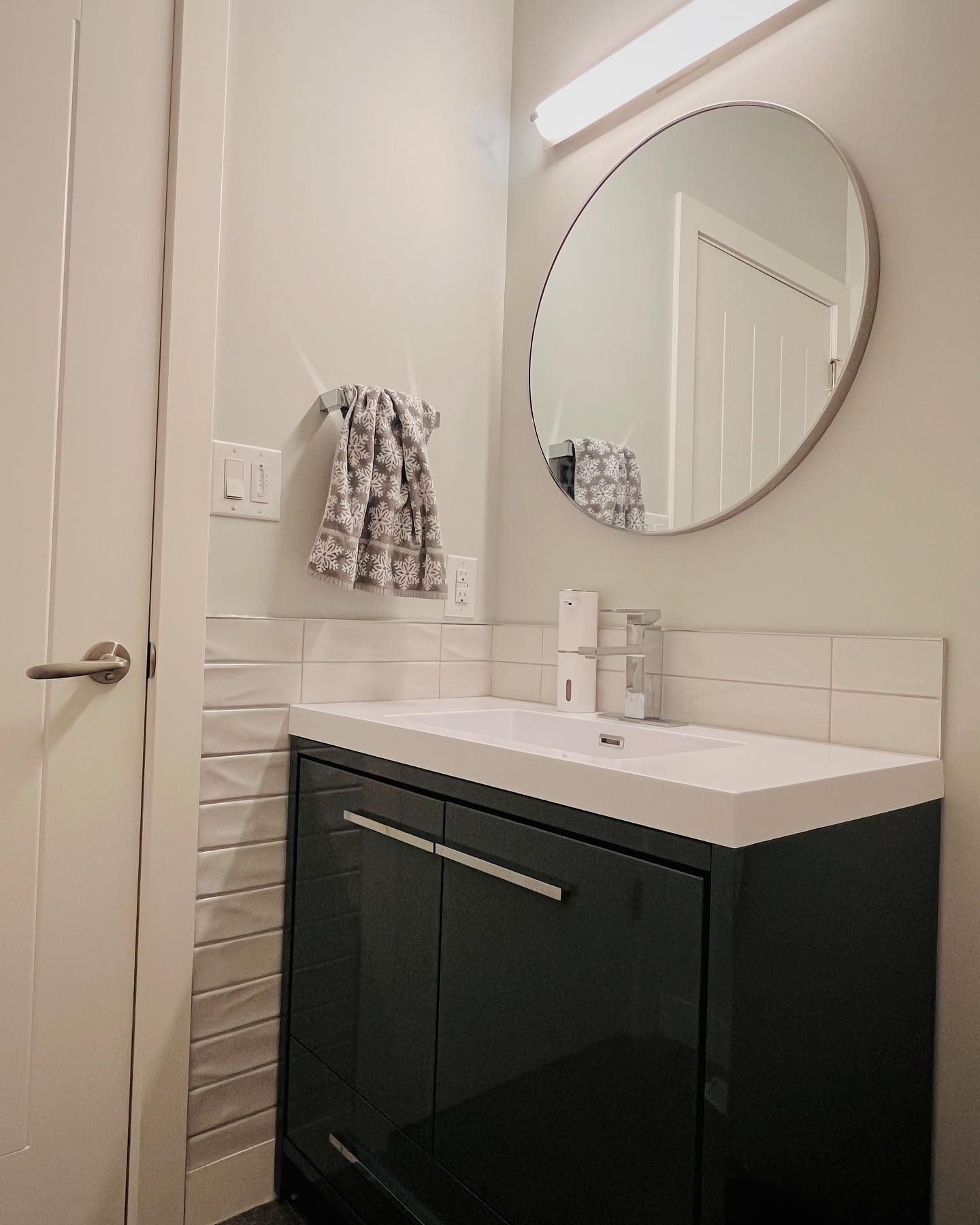 Bathroom vanity in dark gloss with a white sink, circular mirror, and linear sconce