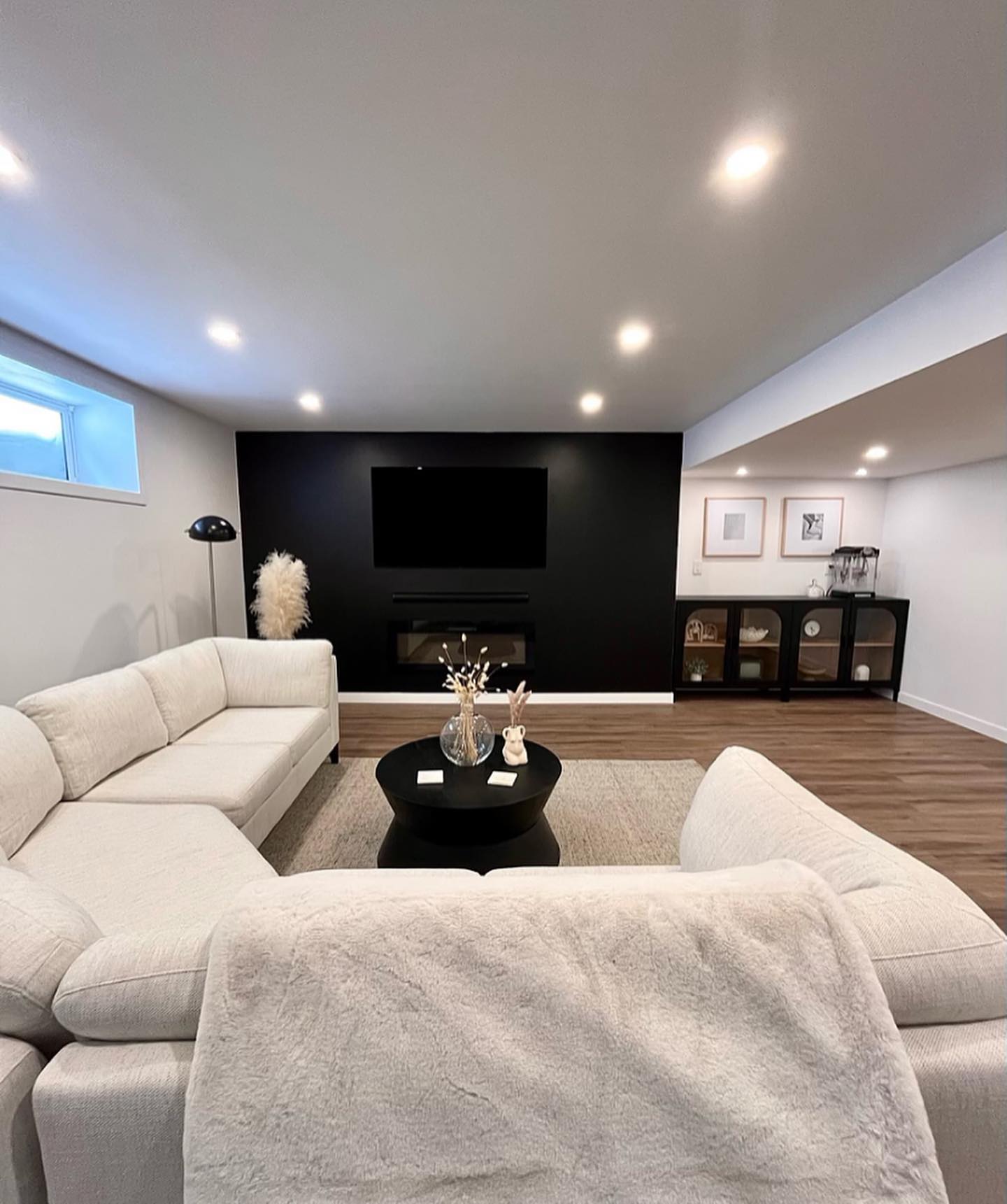 Basement lounge with a cream sectional, black fireplace wall, and a round coffee table