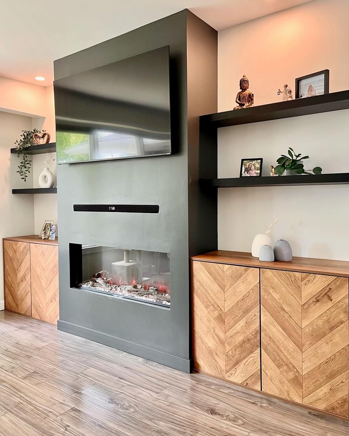 Living room fireplace wall with herringbone wood cabinets and black shelves