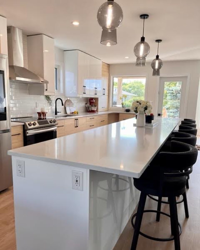 Kitchen island with glossy white drawers, black stools, wood pantry cabinets, and glass pendants