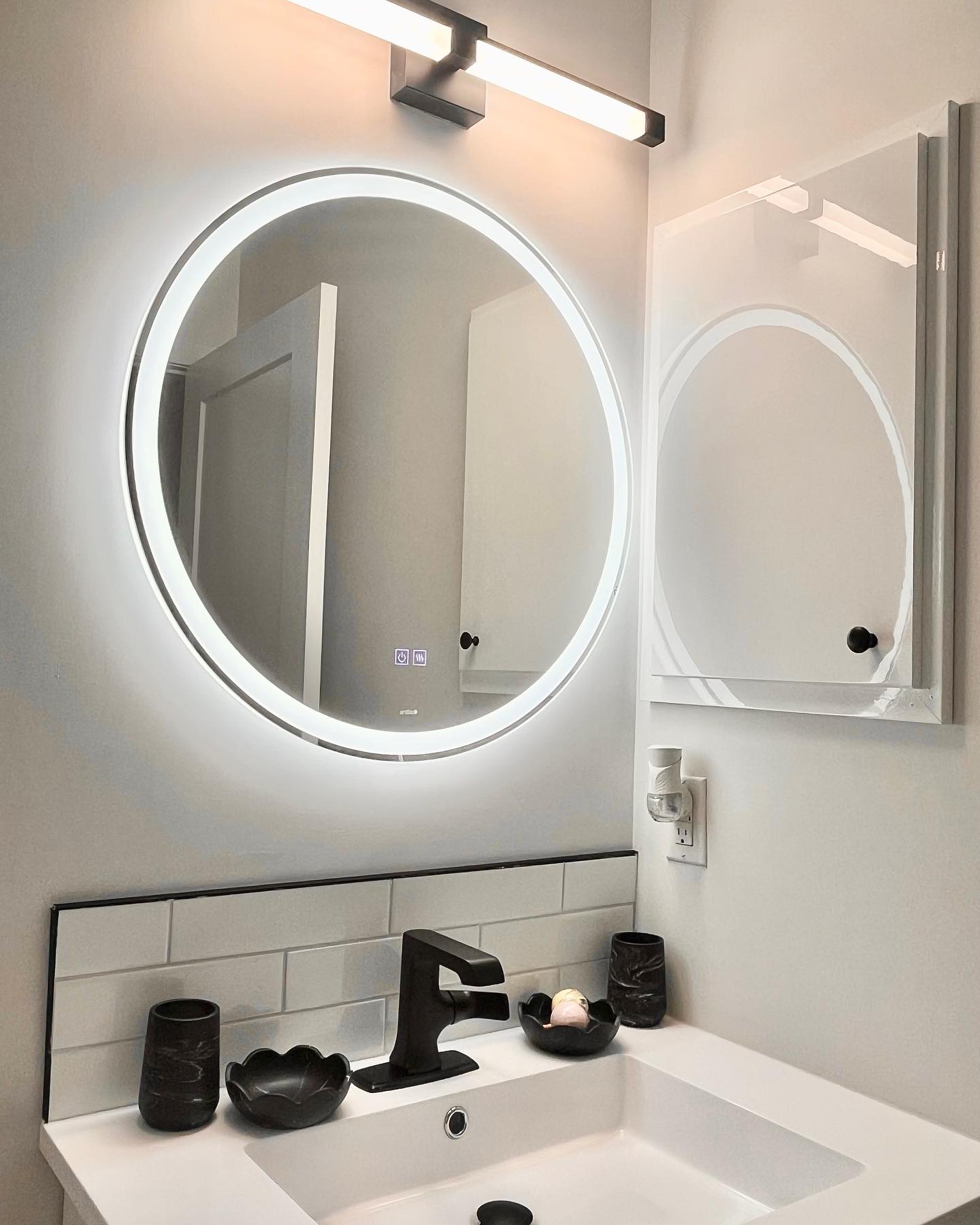 Bathroom vanity with a backlit round mirror, matte black faucet, and a linear sconce