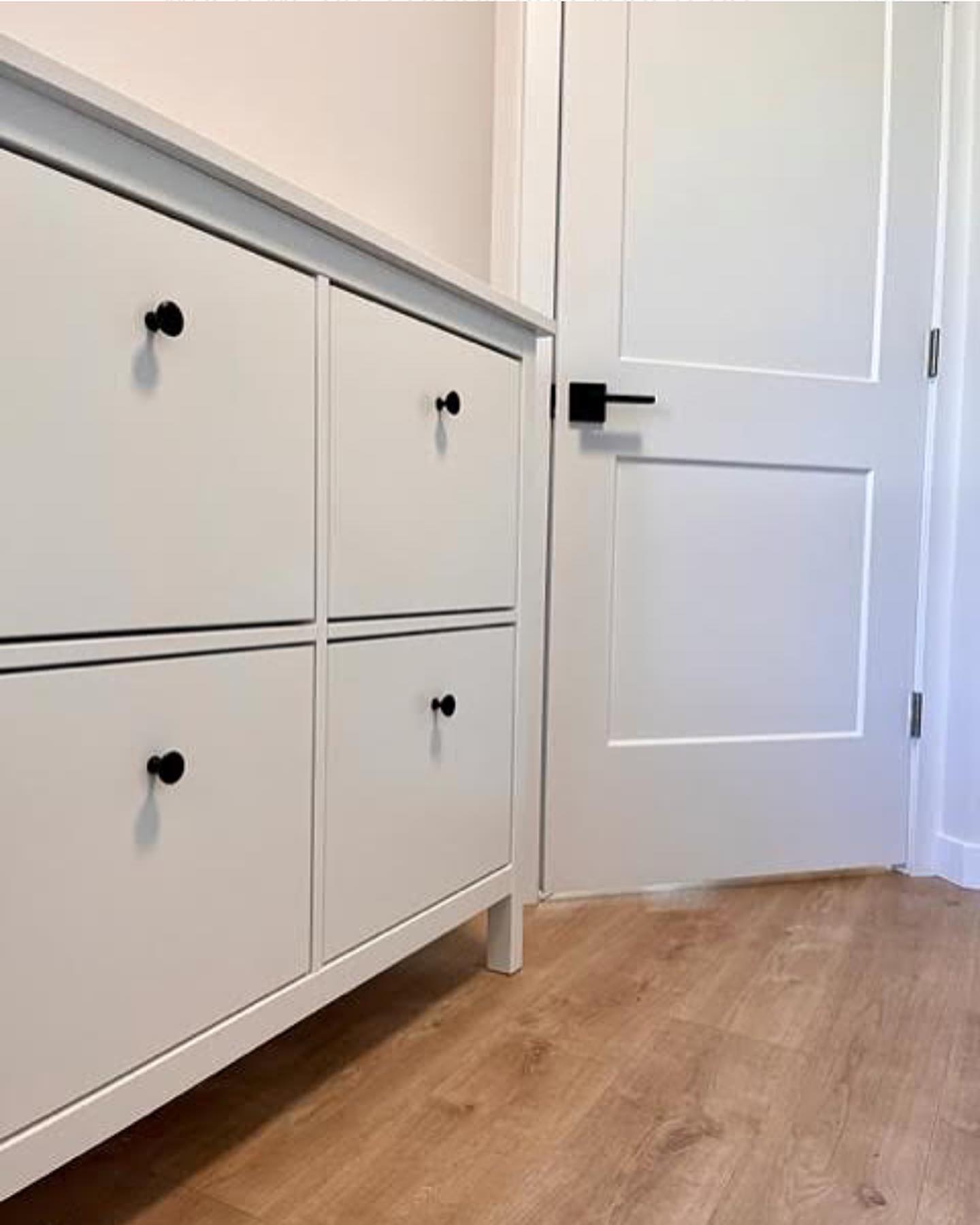 Entry shoe cabinet in white with matte black knobs beside a shaker door