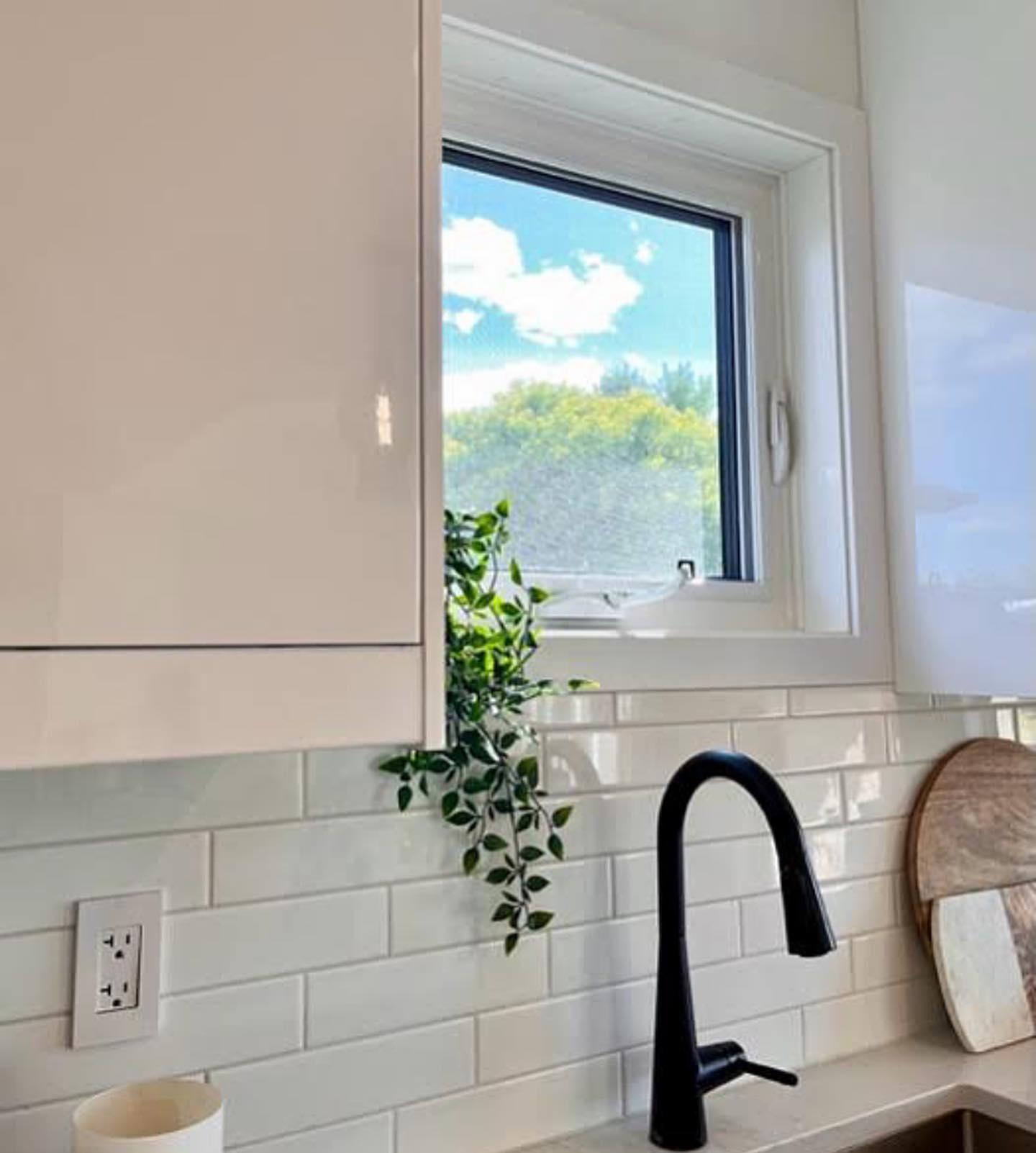 Kitchen sink under a window, with glossy white cabinets and a matte black faucet