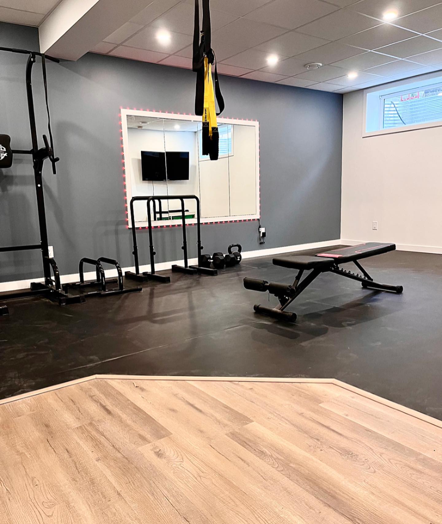 Home gym with a slate wall, backlit mirror, rubber mats, and organized equipment