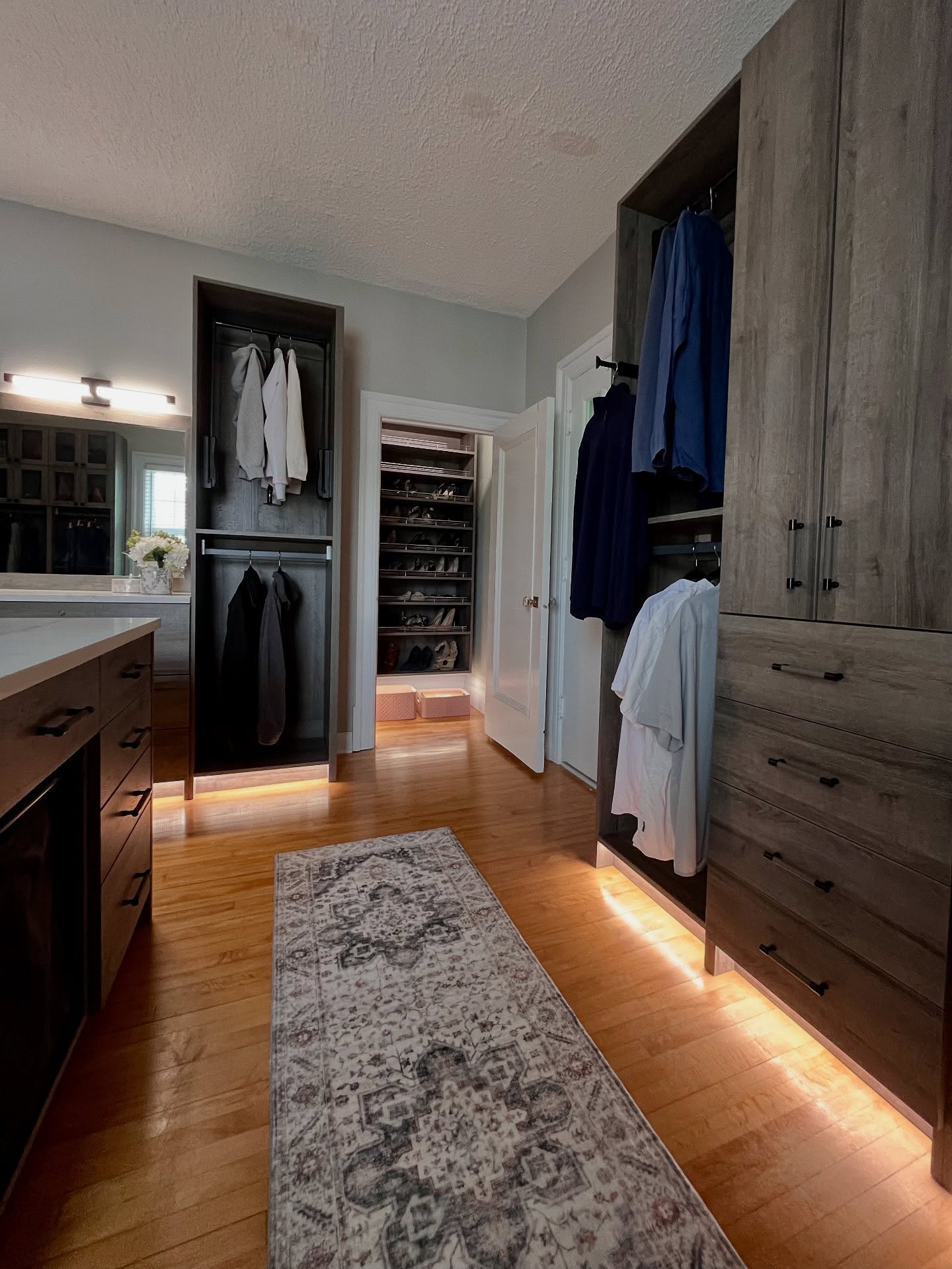 Walk-in closet with dark wood cabinets, a long runner, and warm toe-kick lighting