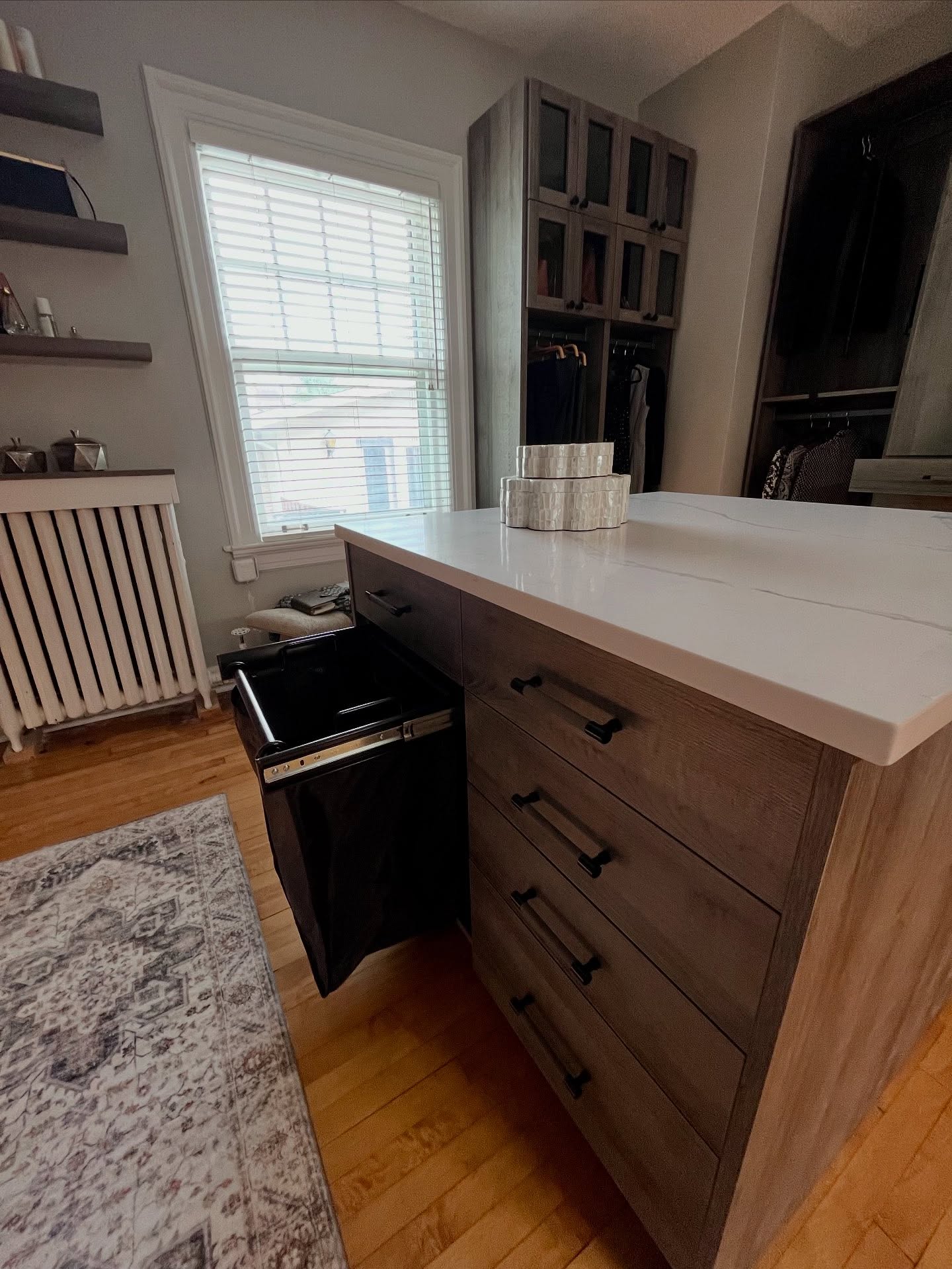 Closet island with a white quartz top, wood drawers, and an open laundry hamper