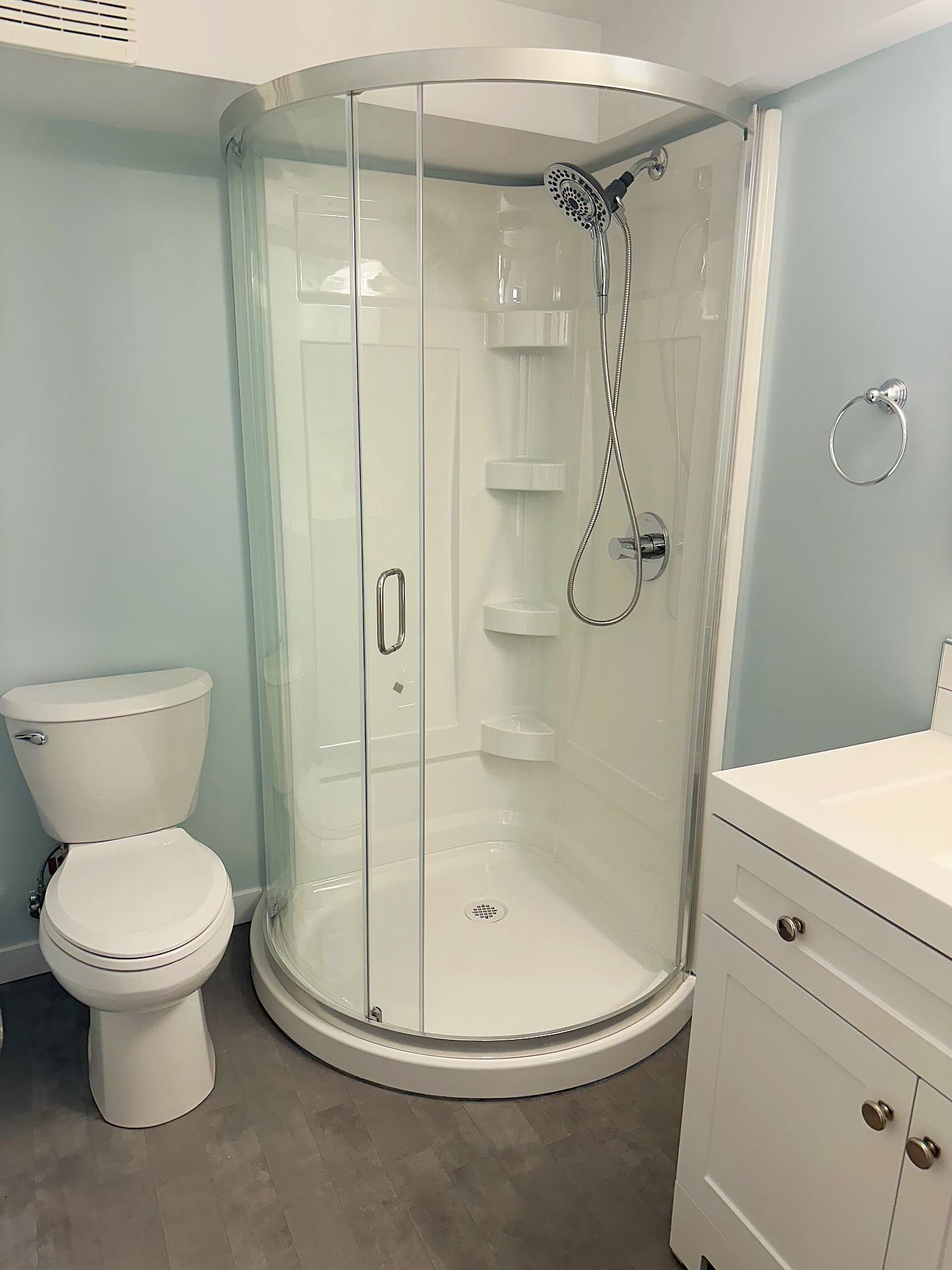 Compact bathroom with a curved-glass corner shower, white vanity, and grey floor tile